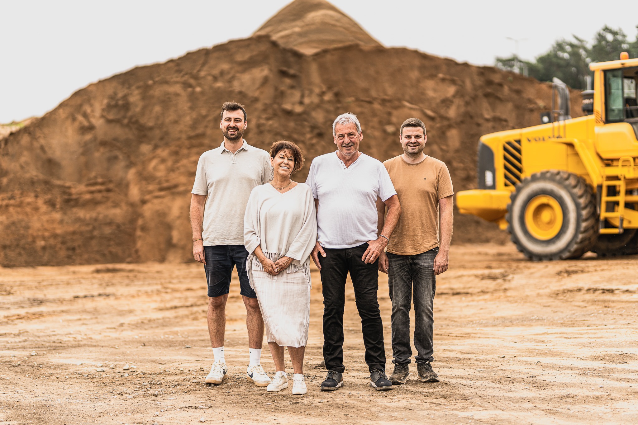 Vierköpfiges Team eines Familienunternehmens vor einem Sandhaufen mit Radlader im Hintergrund