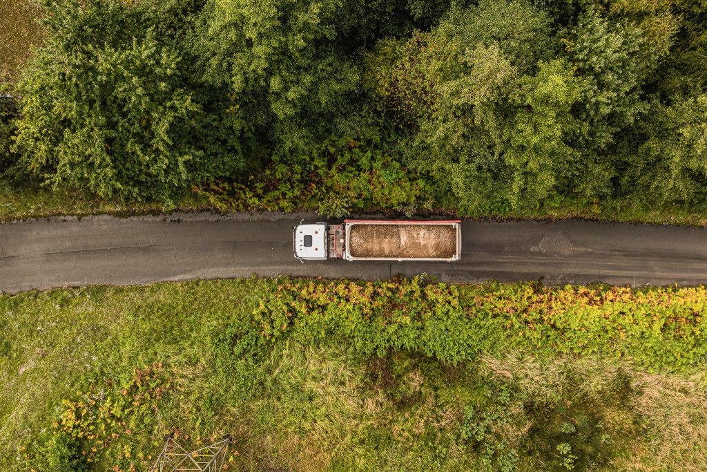 Lkw mit Erdmaterial fährt auf einer schmalen Straße durch bewachsene Landschaft