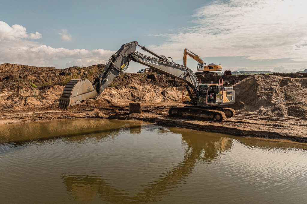 Bagger beim Aushub von Erdmaterial an Gewässer auf einer Baustelle