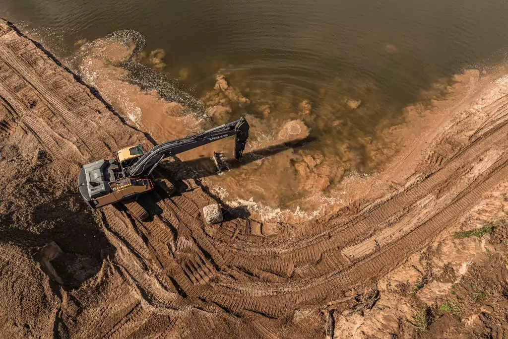 Bagger arbeitet am Ufer eines Gewässers und bewegt Erdmaterial im Wasser